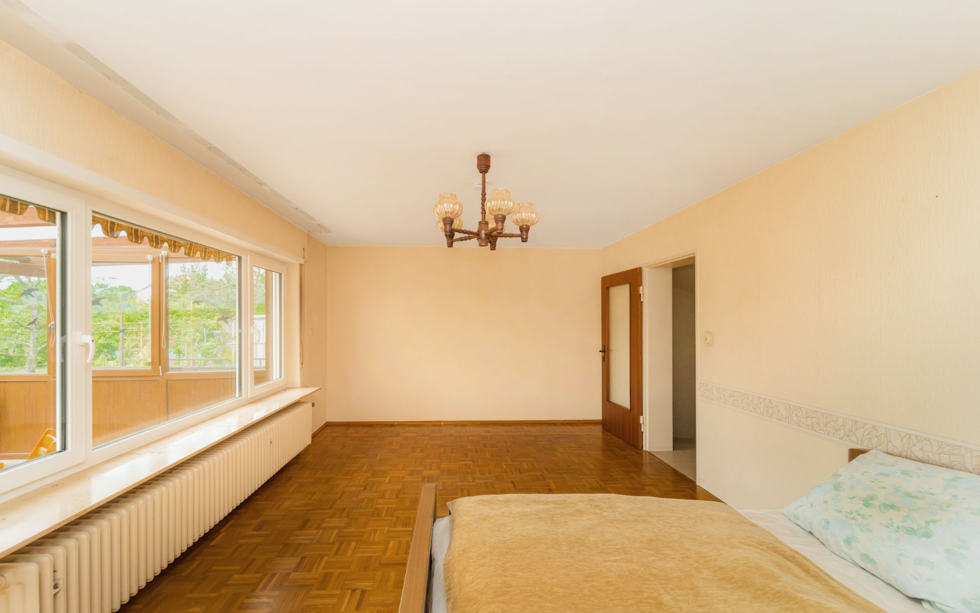 Helles Schlafzimmer mit großem Fenster, Holzboden, Bett und Kronleuchter.