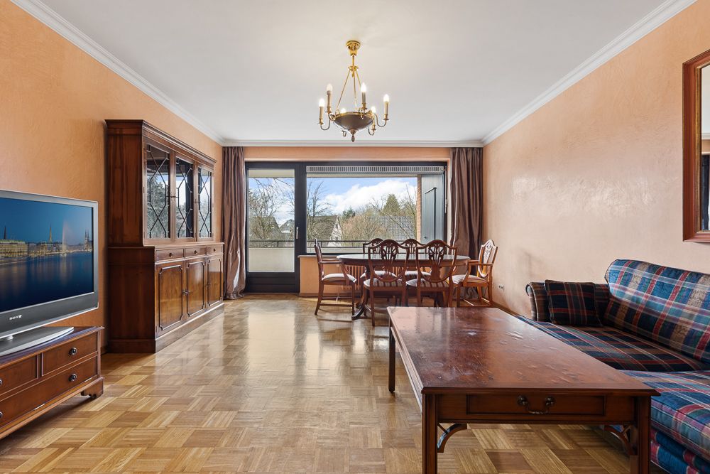 Wohnzimmer mit Holzmöbeln, einem Esstisch, Sofa, Fernseher und großem Fenster mit Aussicht.