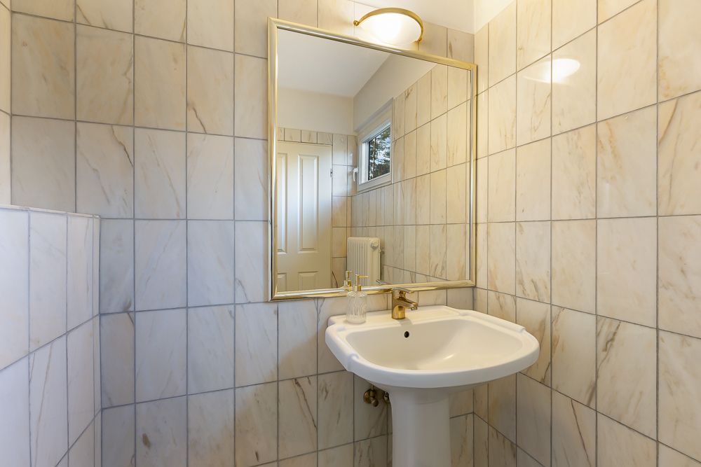 Kleines Badezimmer mit Waschbecken, Spiegel und gefliesten Wänden.