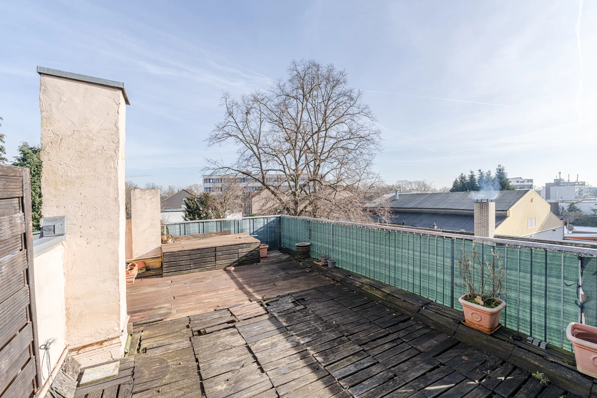 Dachterrasse mit Holzboden, Pflanzkübeln und Ausblick auf Bäume und Nachbargebäude.