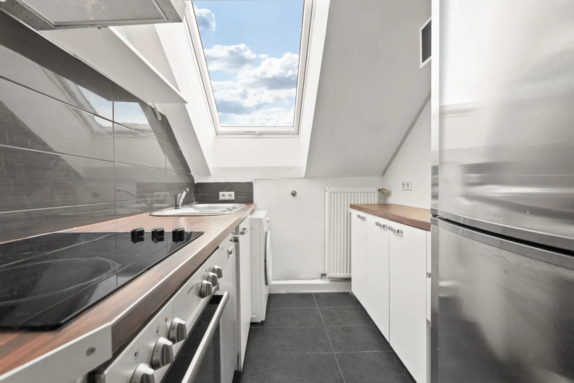 Moderne, schmale Küche mit Dachfenster, Elektroherd, Spüle und Edelstahlkühlschrank.