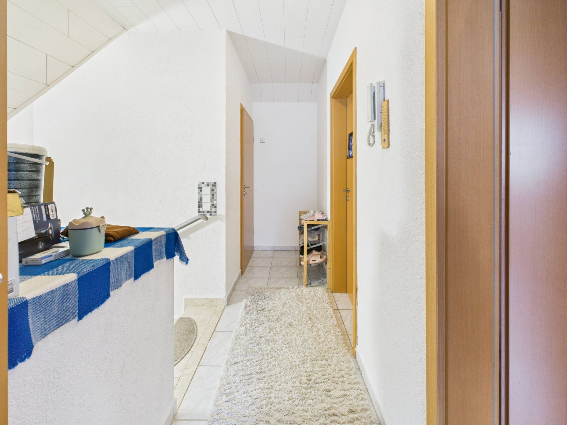 Heller Flur mit Teppich, Holztüren und einem Regal, weiße Wände und Decke.