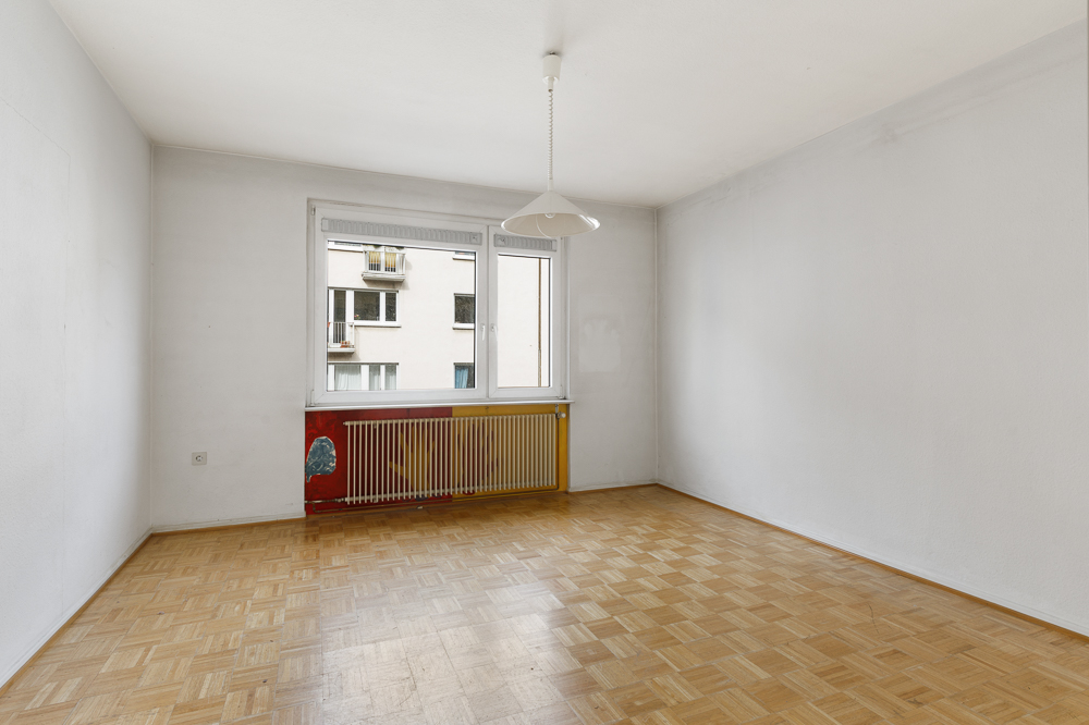 Leerer Raum mit Parkettboden, weißem Wänden, Fenster und Heizkörper unter dem Fenster.