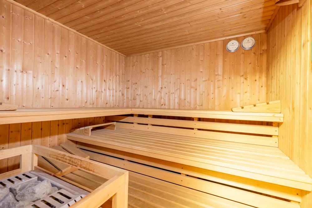 Innenansicht einer Sauna mit Holzbänken, Holzwänden und zwei Messgeräten an der Wand.
