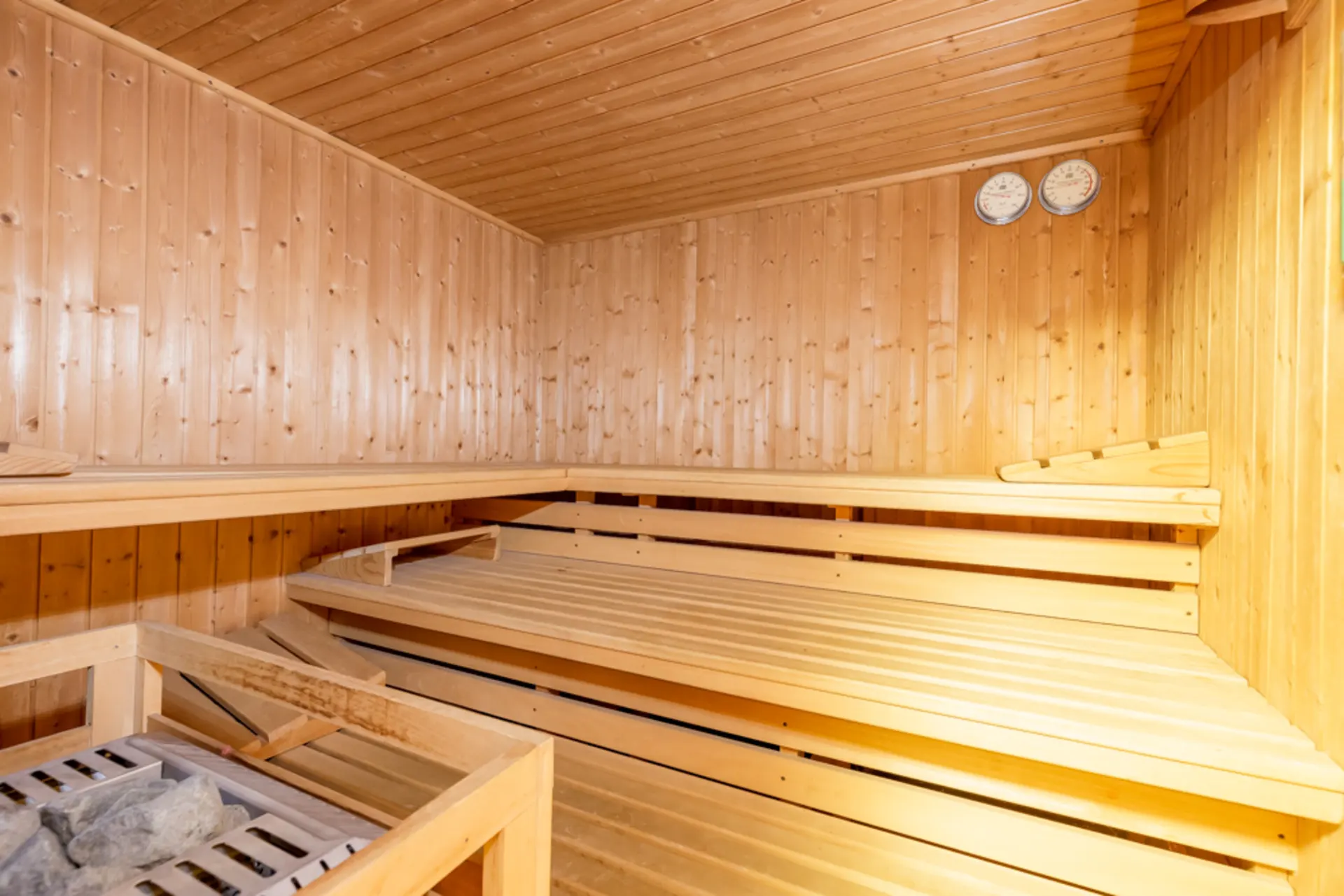 Innenansicht einer Sauna mit Holzbänken, Holzwänden und zwei Messgeräten an der Wand.