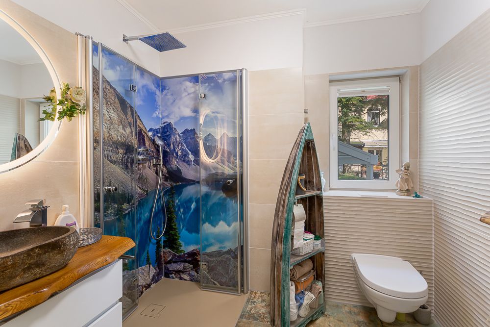 Modernes Bad mit Waschbecken, Dusche mit Naturmotiv und WC, Regal in Bootsform, Fenster mit Ausblick.