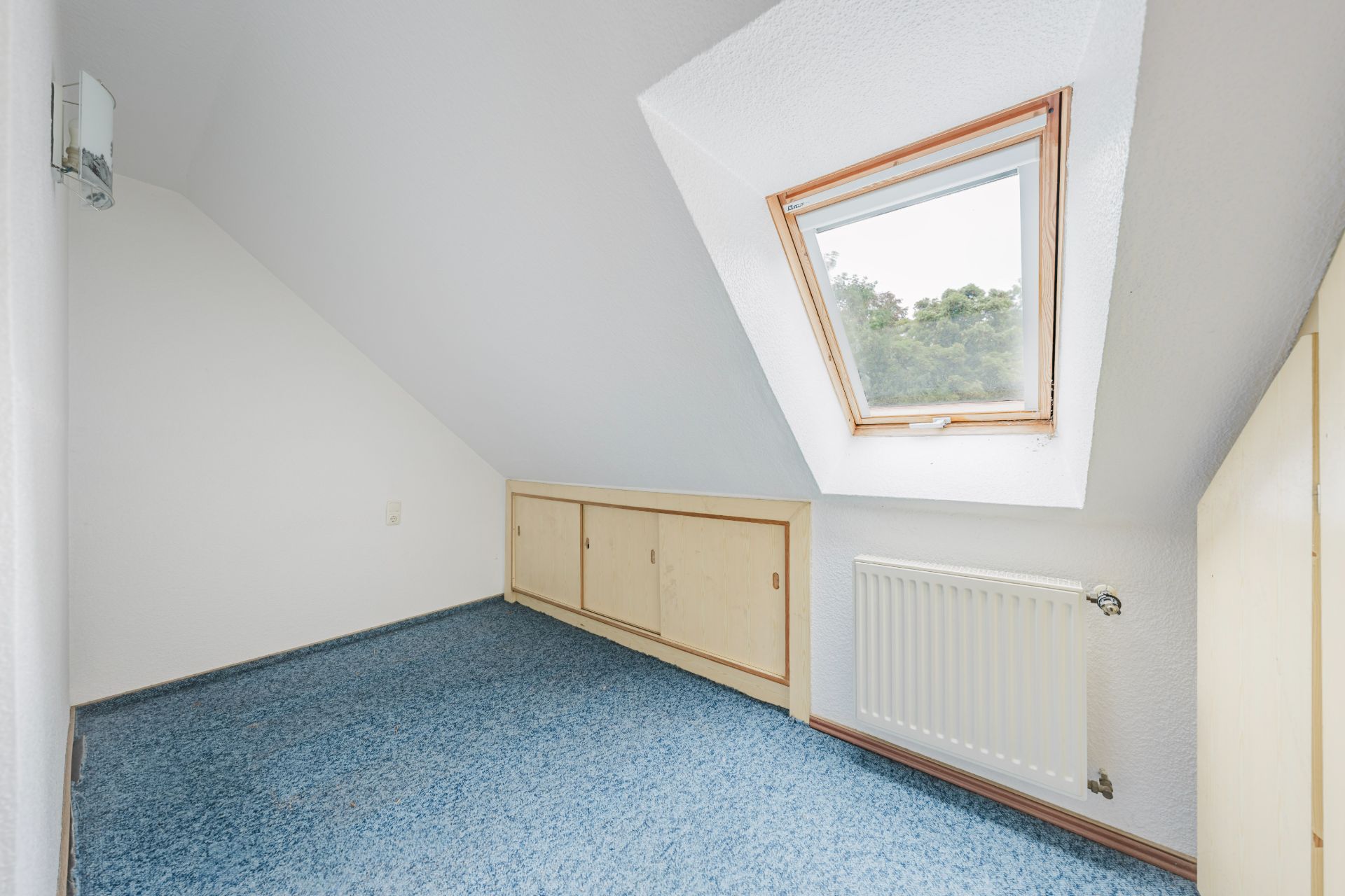 Kleiner Raum mit blauer Teppich, Dachfenster und Einbauschränken unter der Schräge.