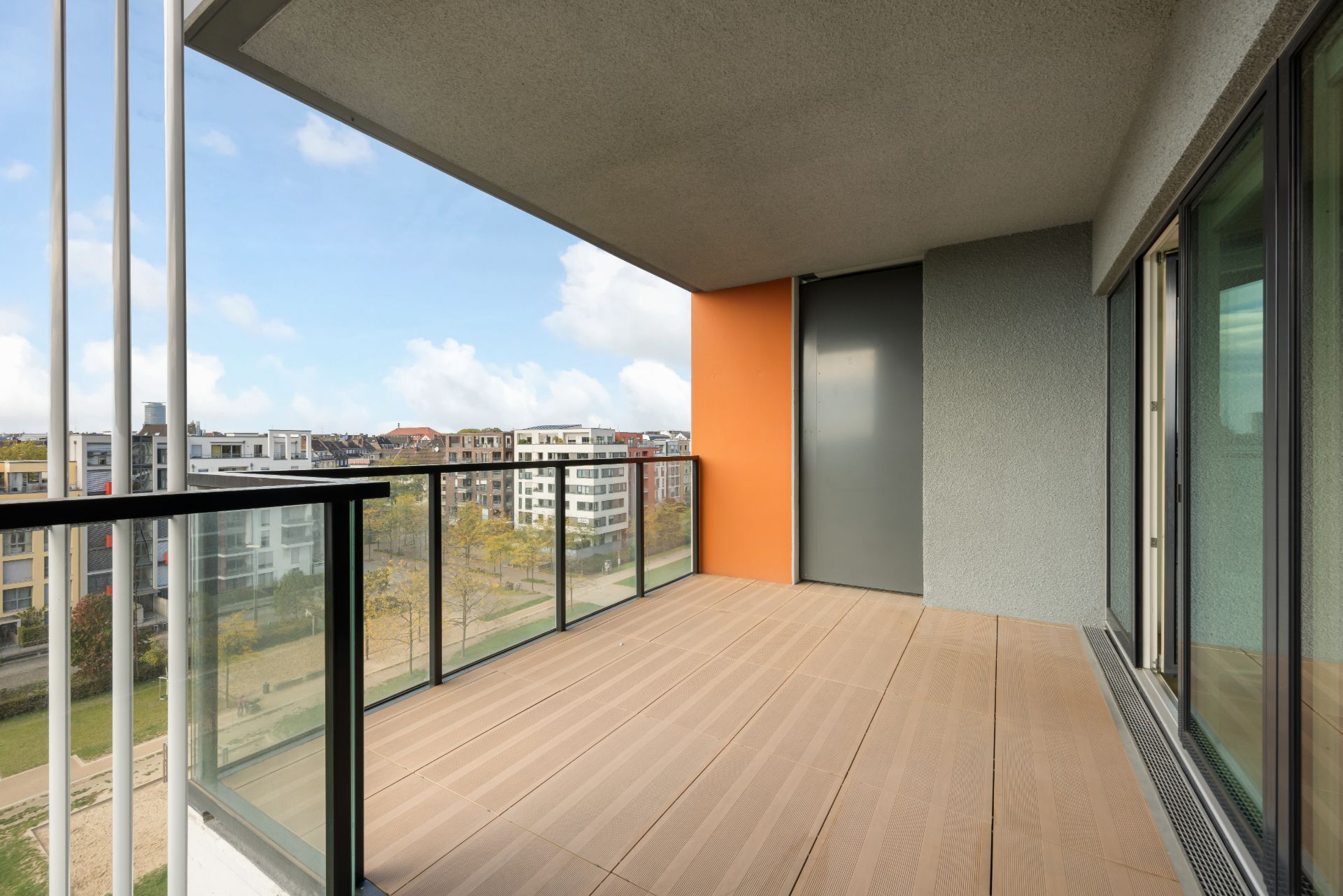 Moderner Balkon mit Glasgeländer und Blick auf Wohngebäude.