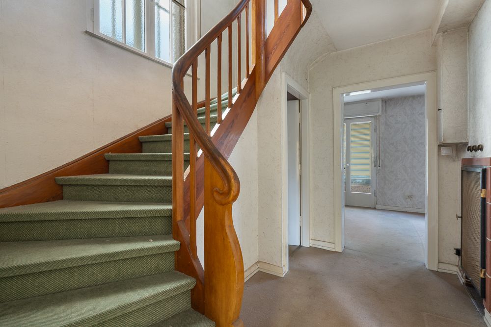 Treppenhaus mit grünem Teppich, Holzgeländer und angrenzendem Flur in einem Wohnhaus.