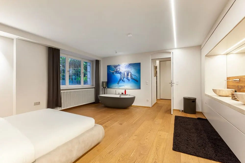 Modernes Schlafzimmer mit freistehender Badewanne, großem Fenster und Holzboden.