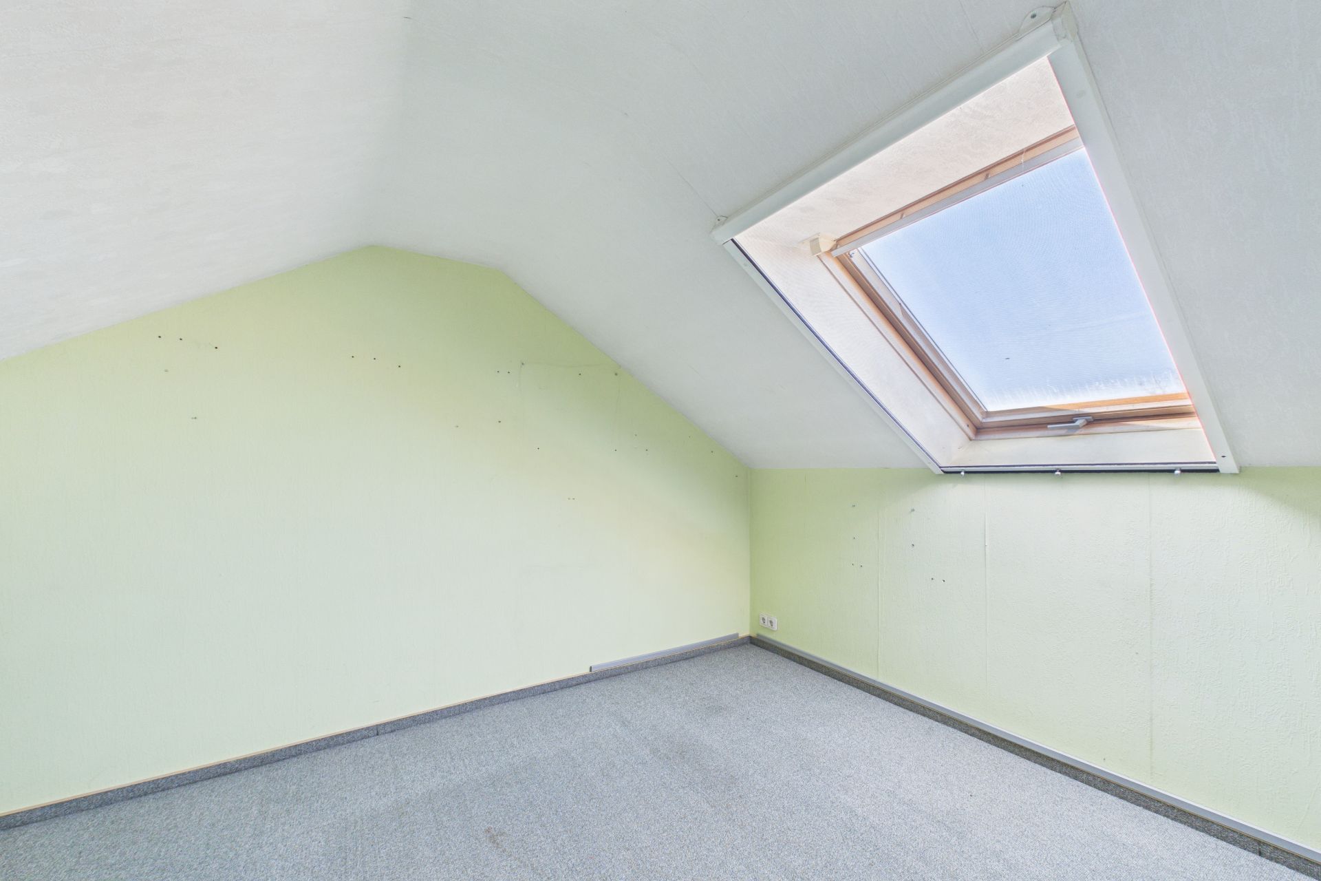 Heller Raum mit Dachschräge, grün gestrichenen Wänden und großem Dachfenster.