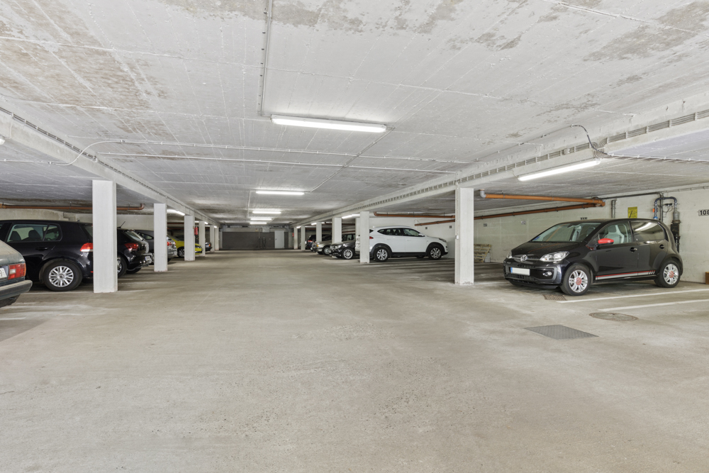 Helle Tiefgarage mit mehreren geparkten Autos und Betonpfeilern.