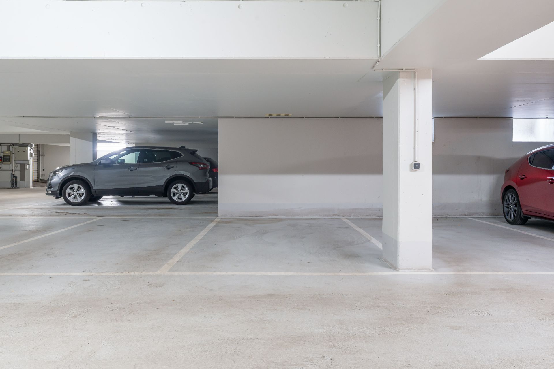 Tiefgaragenstellplätze mit einem grauen und einem roten Auto, leere Parklücke in der Mitte.