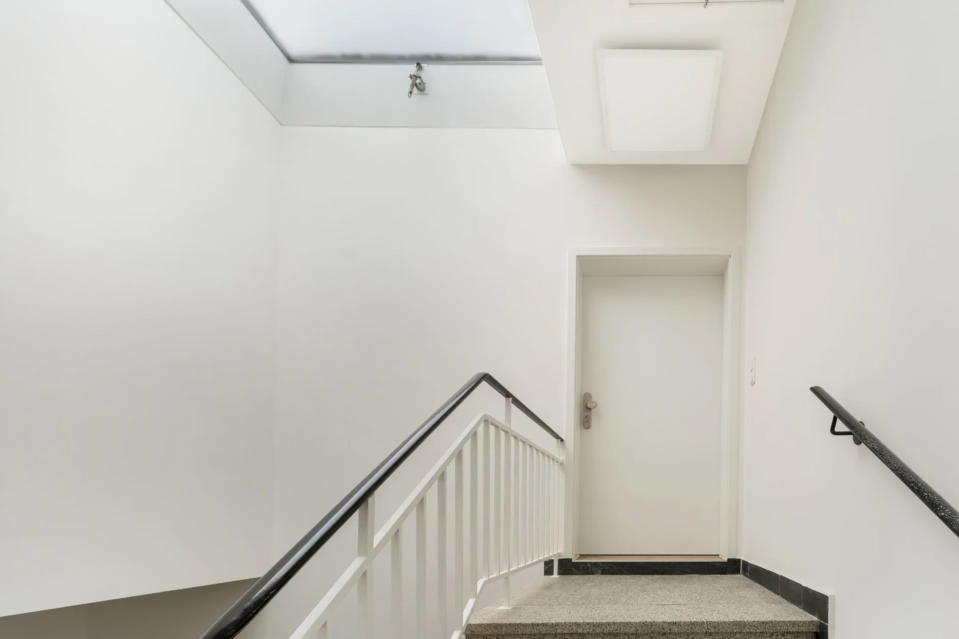 Helle Treppe mit weißer Tür am oberen Ende und einem Oberlicht an der Decke.