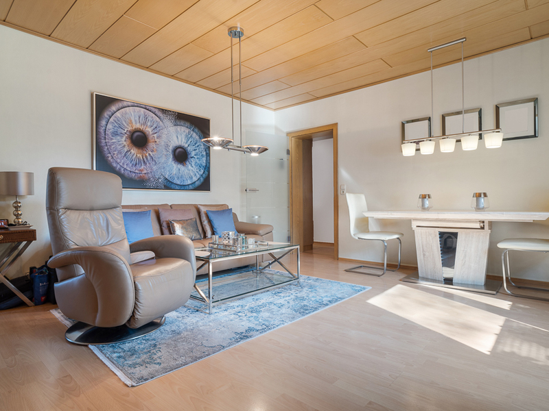 Modernes Wohnzimmer mit Ledersessel, Sofa, Glastisch, Teppich und Esstisch mit Stühlen.
