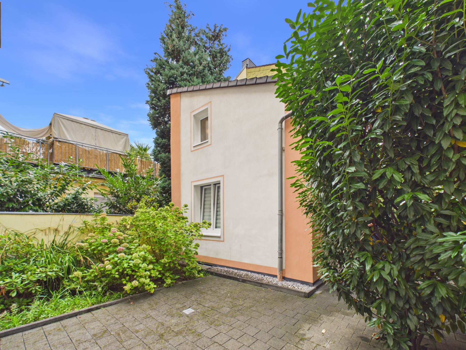 Kleines Haus mit gepflastertem Hof und viel Grün im Garten.
