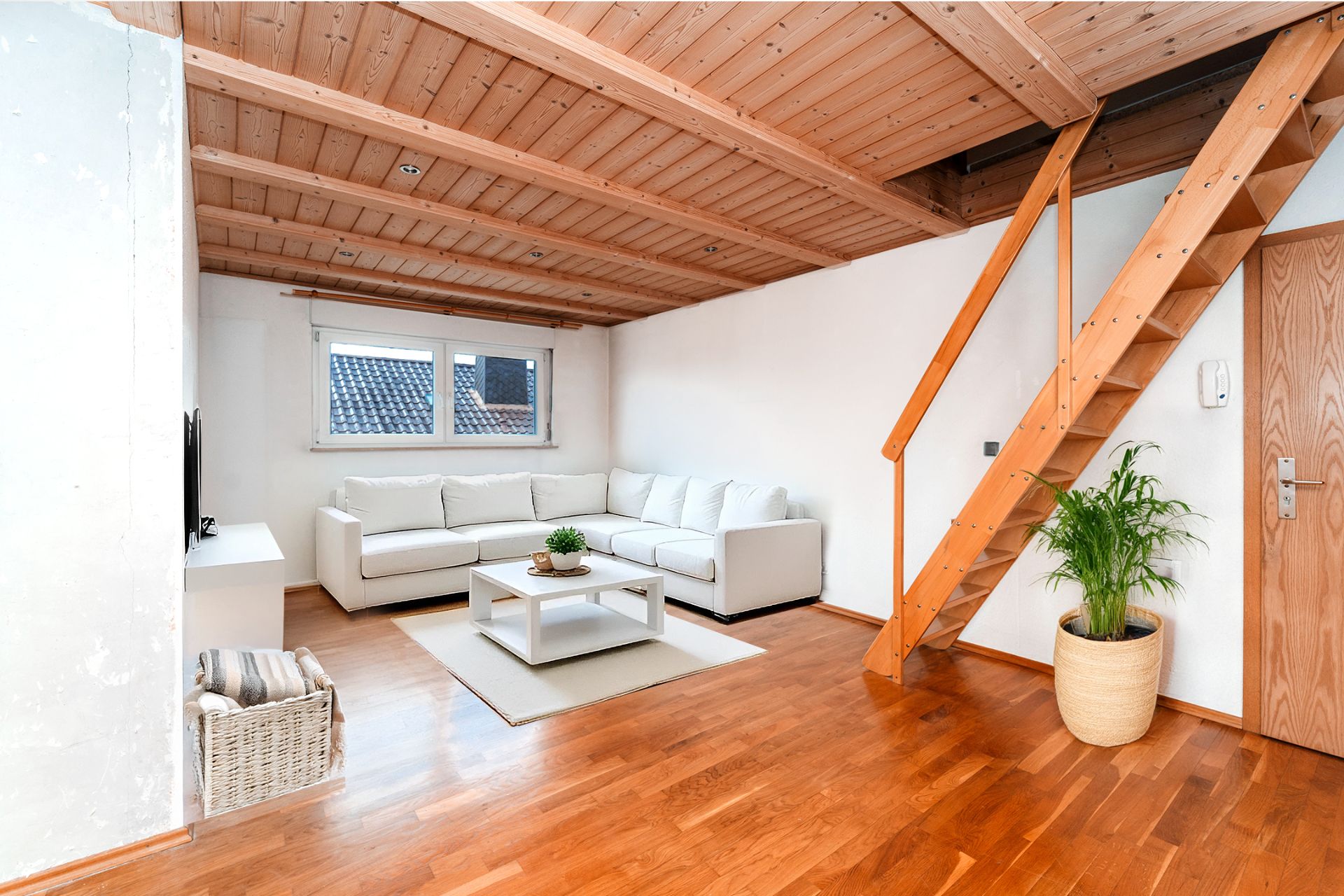 Helles Wohnzimmer mit weißem Sofa, Couchtisch, Pflanze und Holztreppe zu einer Empore.