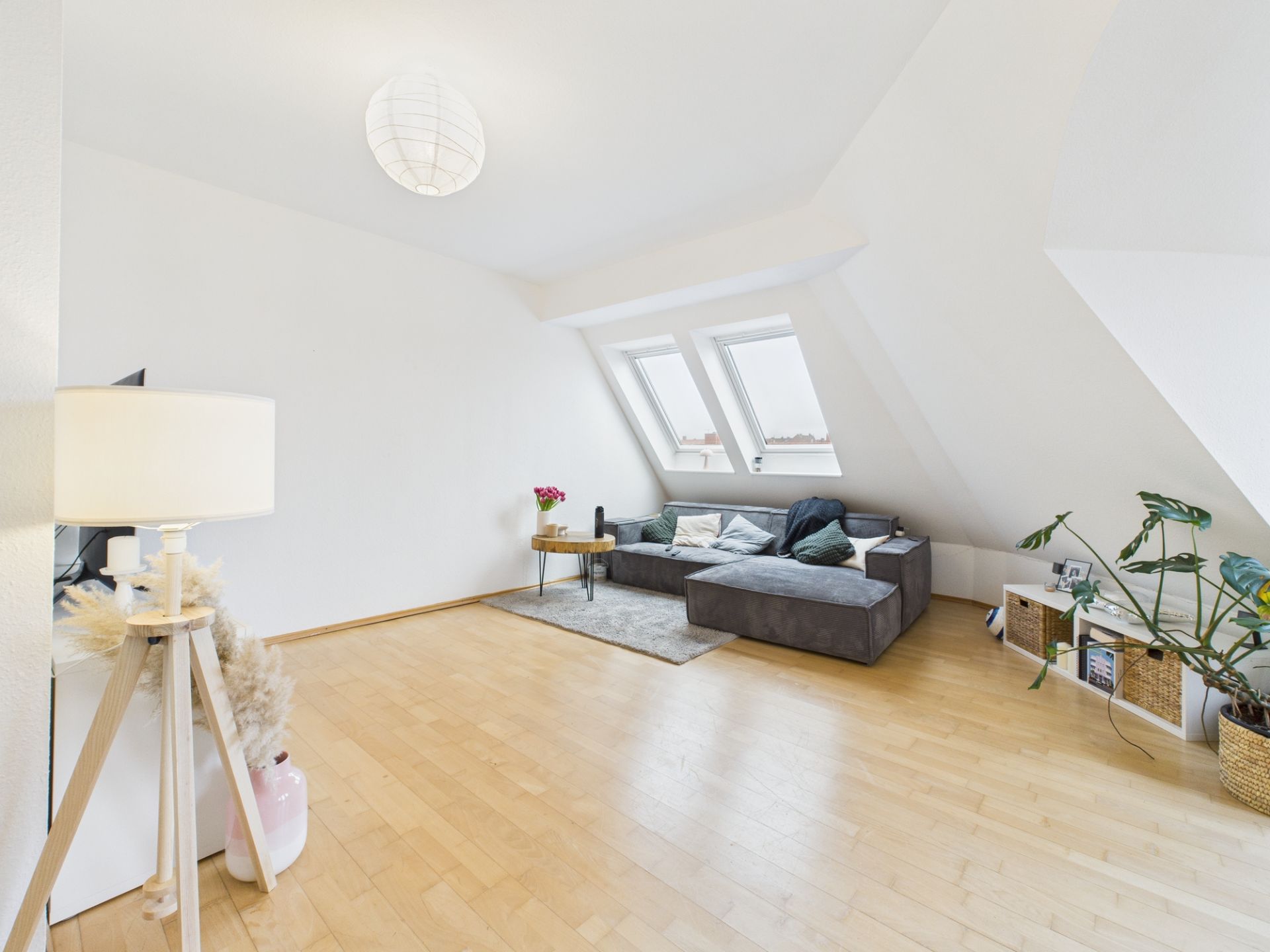 Helles Wohnzimmer mit Dachschräge, Holzfußboden, Sofa, Pflanzen und Stehlampe.