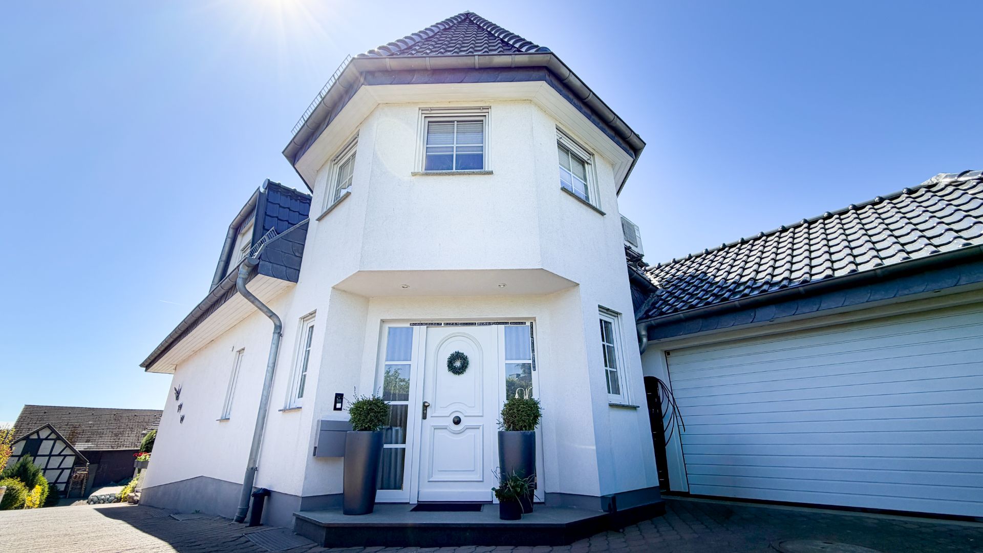 Modernes weißes Einfamilienhaus mit Erker, Eingangsbereich und Garage bei Sonnenschein.