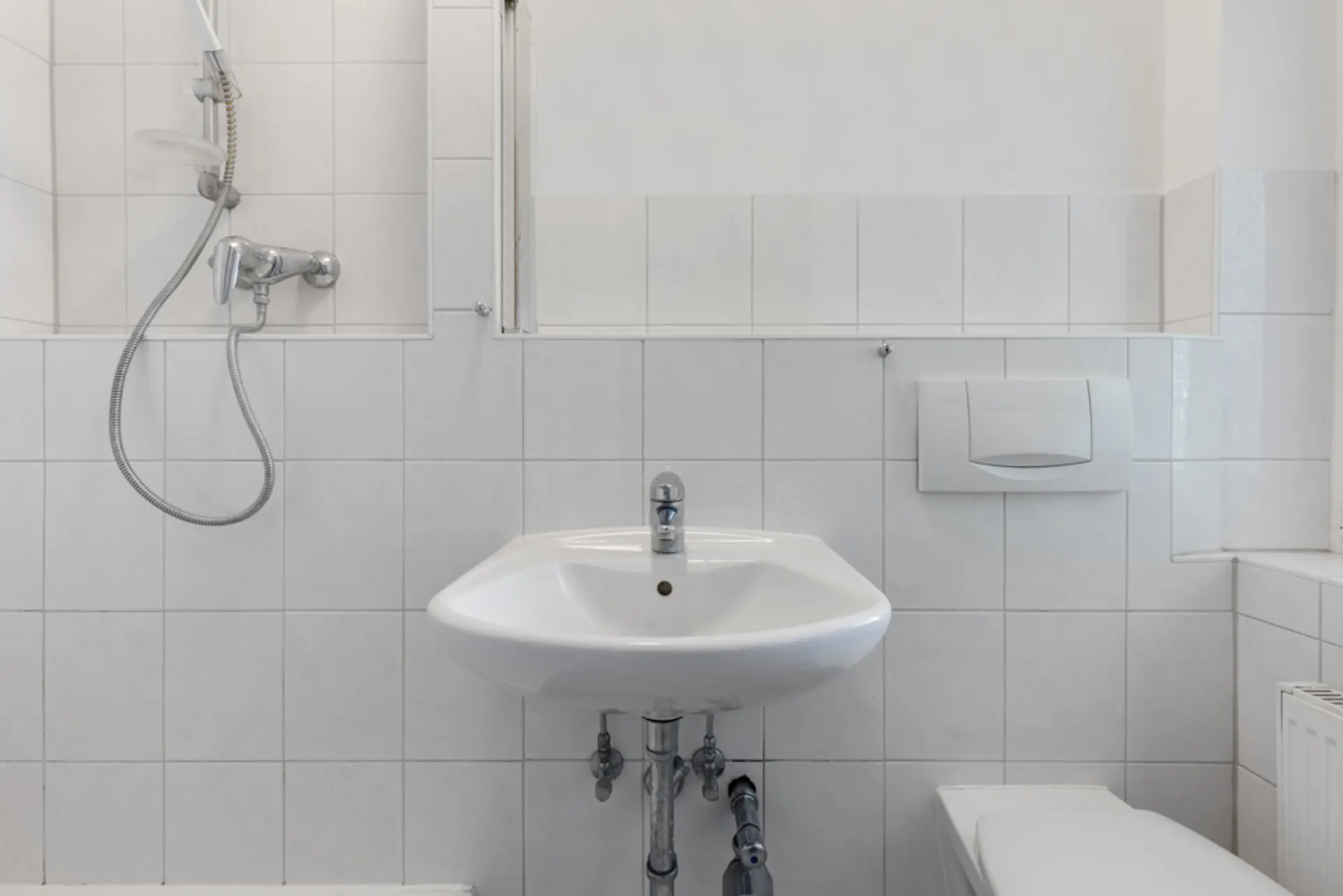 Kleines Badezimmer mit Waschbecken, Dusche und Toilette, weiße Fliesen an den Wänden.