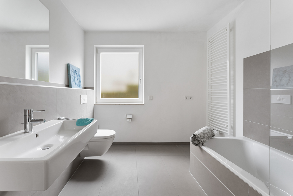 Modernes Badezimmer mit Waschbecken, WC, Badewanne, Fenster und Handtuchheizkörper.