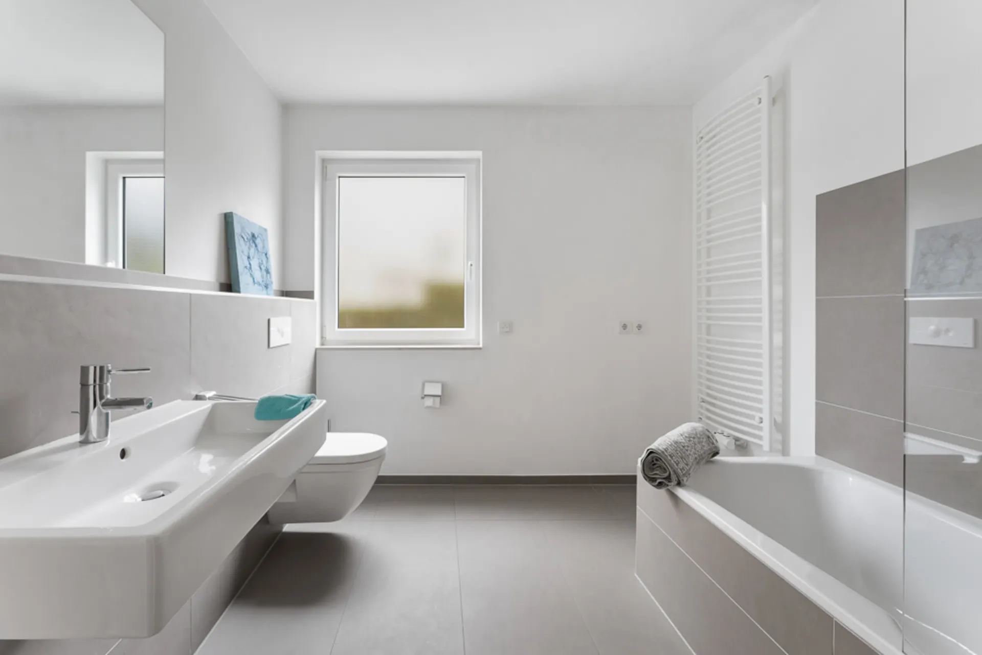 Modernes Badezimmer mit Waschbecken, WC, Badewanne, Fenster und Handtuchheizkörper.