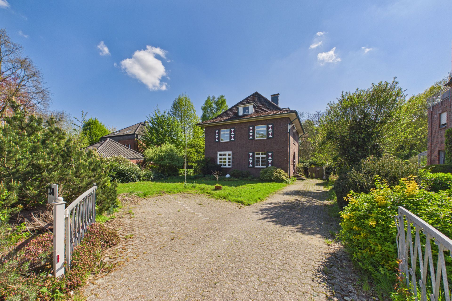 Backsteinhaus mit Dachboden, großem Garten und Einfahrt vor dem Haus, umgeben von Bäumen.