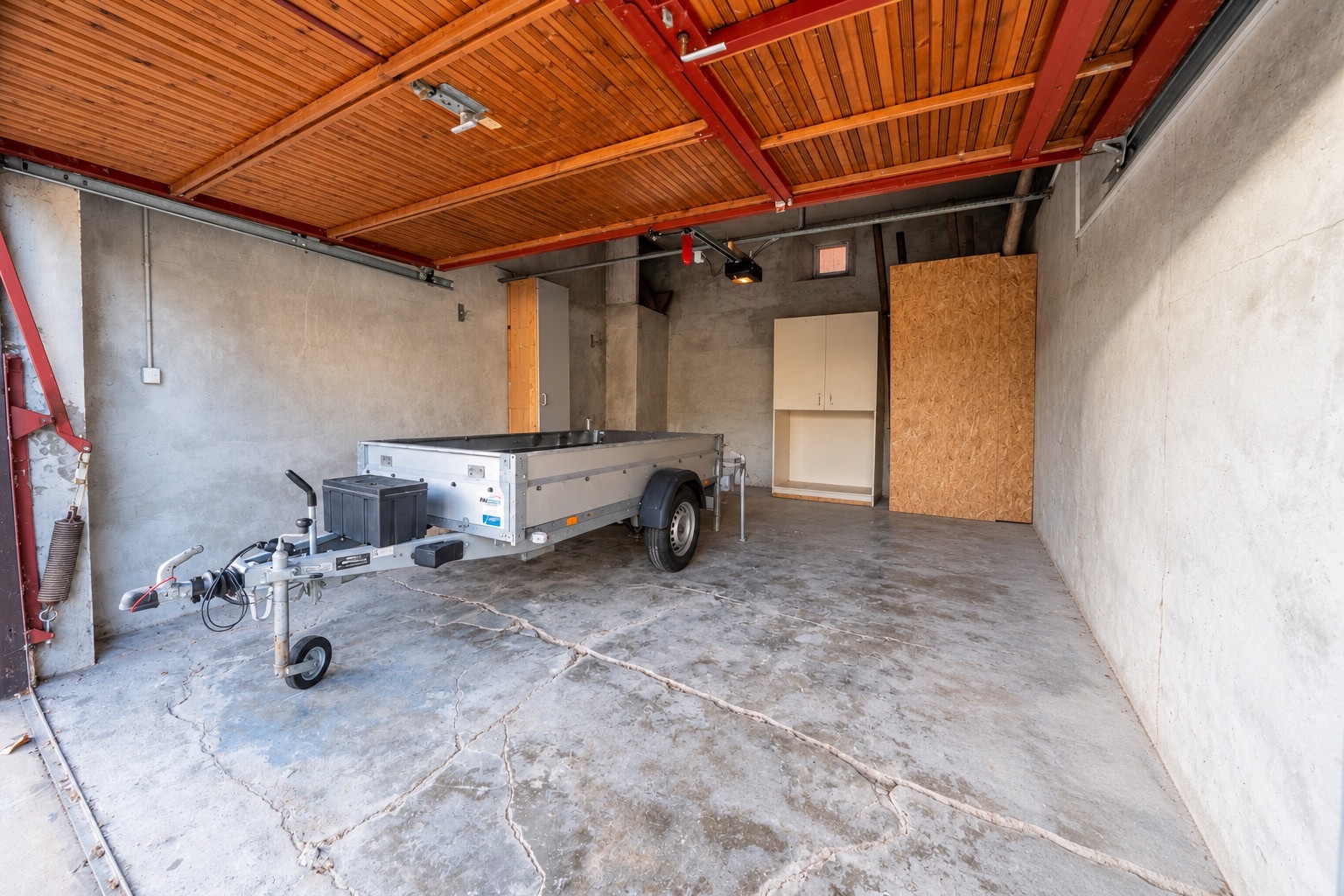 Garage mit offenem Holztor, Anhänger und Schränken an der Rückwand.
