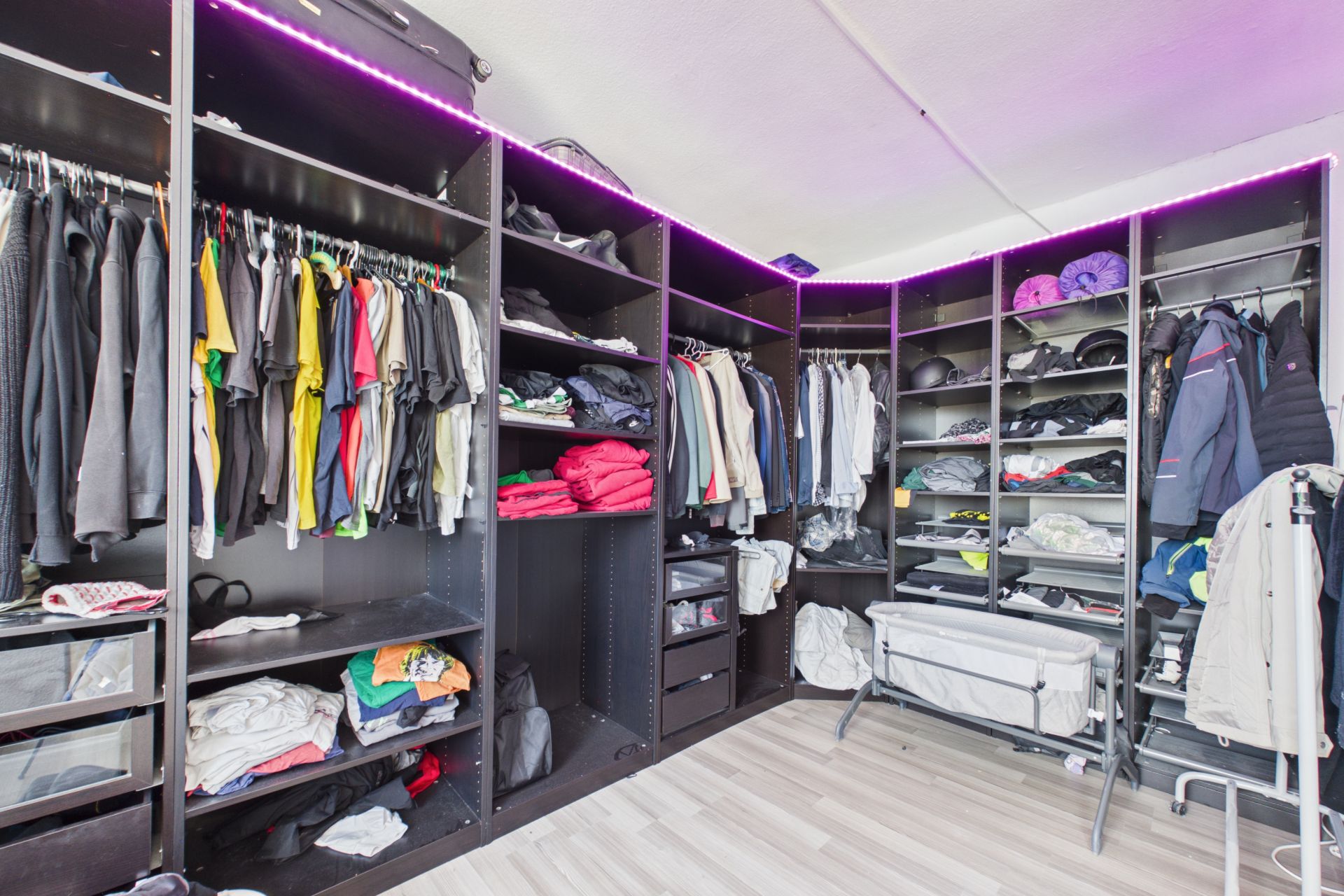 Offener begehbarer Kleiderschrank mit Kleidung, Regalen und aufgehängten Jacken in einem hellen Raum.