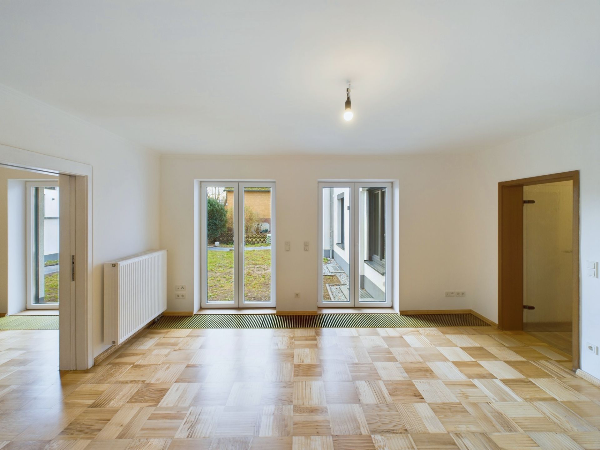 Helles Wohnzimmer mit Parkettboden, großen Fenstern und Zugang zum Garten.