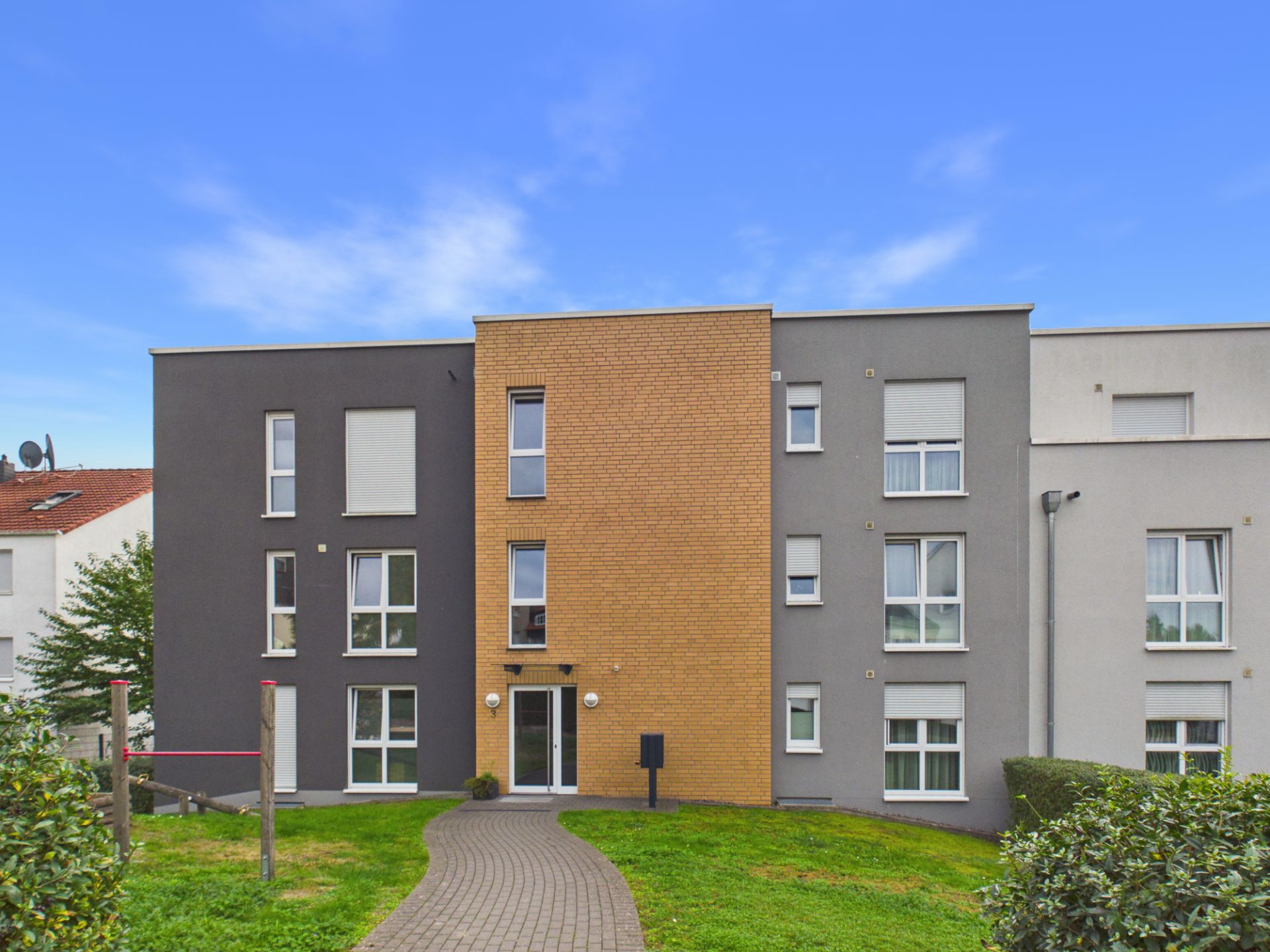 Modernes Wohnhaus mit drei Stockwerken, großem Eingangsbereich und gepflegtem Vorgarten.