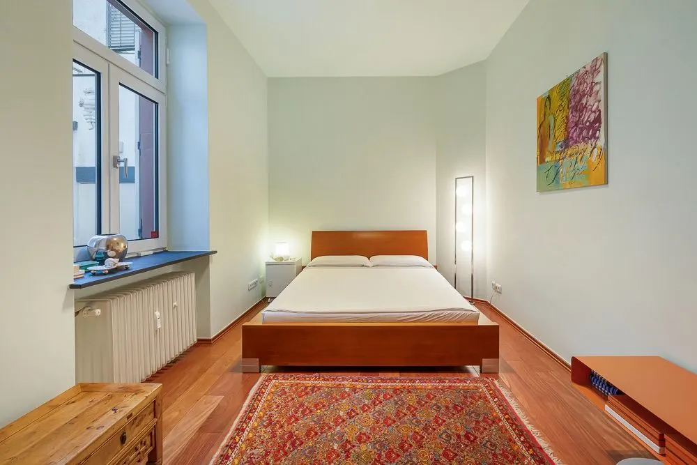 Schlafzimmer mit Doppelbett, Teppich, großem Fenster und Wandbild.