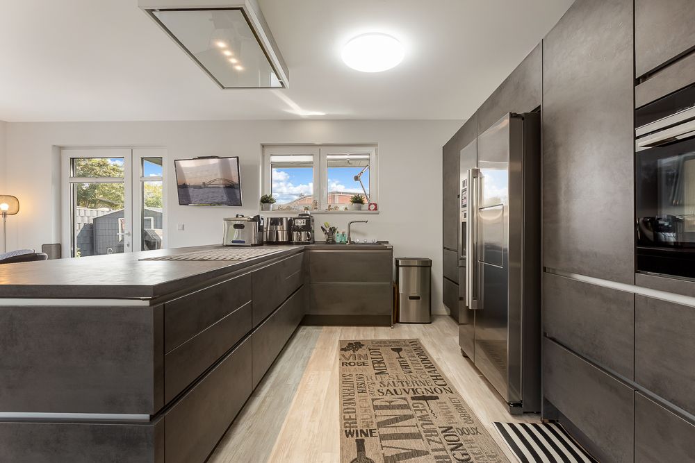 Moderne Küche mit grauen Schränken, Kochinsel, großem Kühlschrank und Fenster.