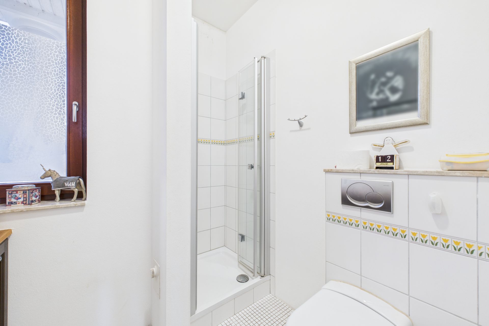 Kleines Bad mit Duschkabine, Toilette, Fenster und wandhängendem Spiegel.