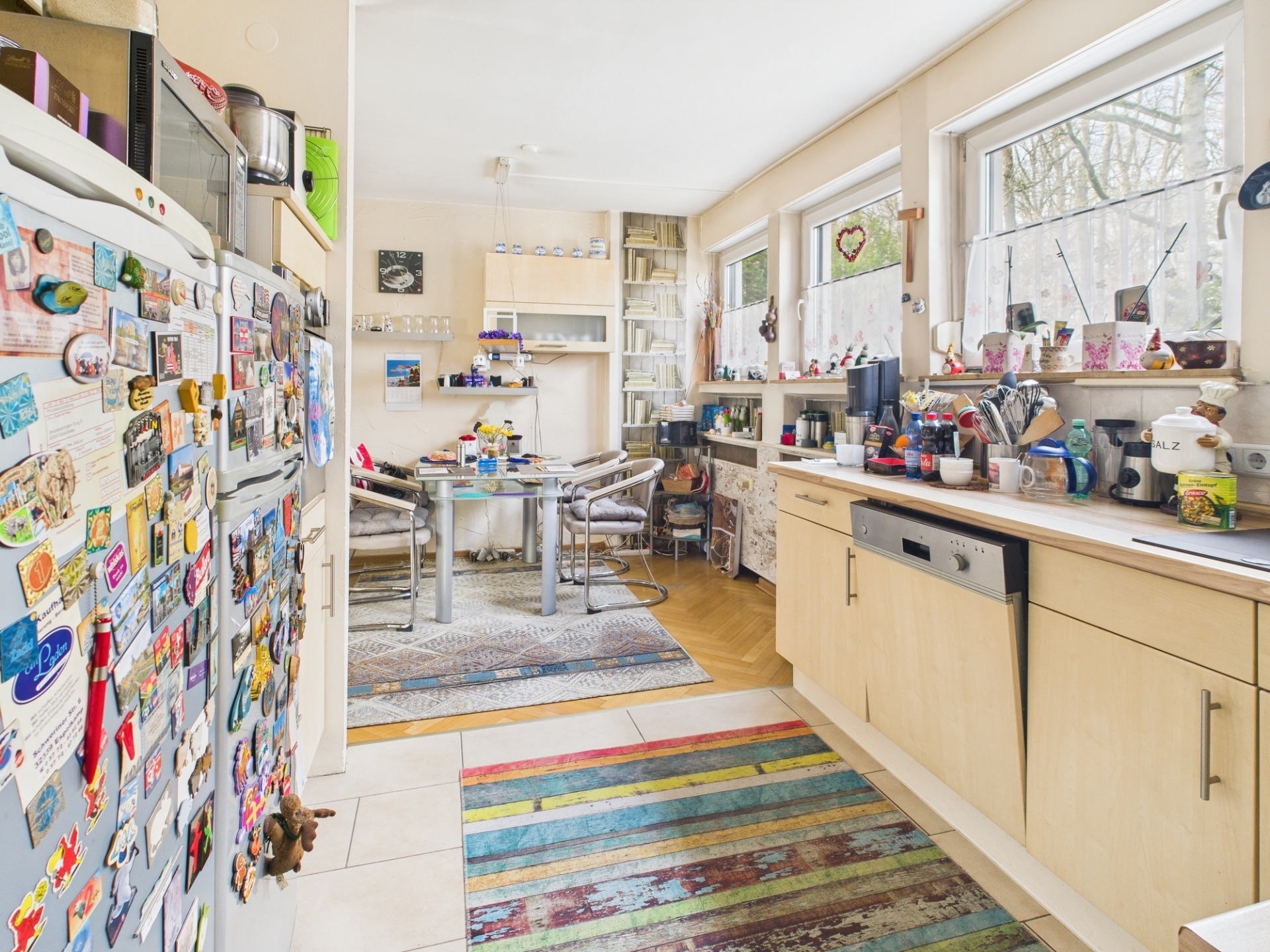 Helle Küche mit buntem Teppich, vielen Magneten am Kühlschrank und Esstisch im Hintergrund.