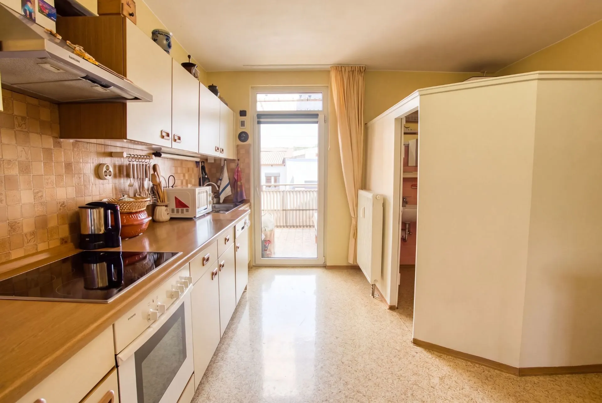 Helle Küche mit Elektroherd, Arbeitsplatte und Zugang zu einem Balkon.