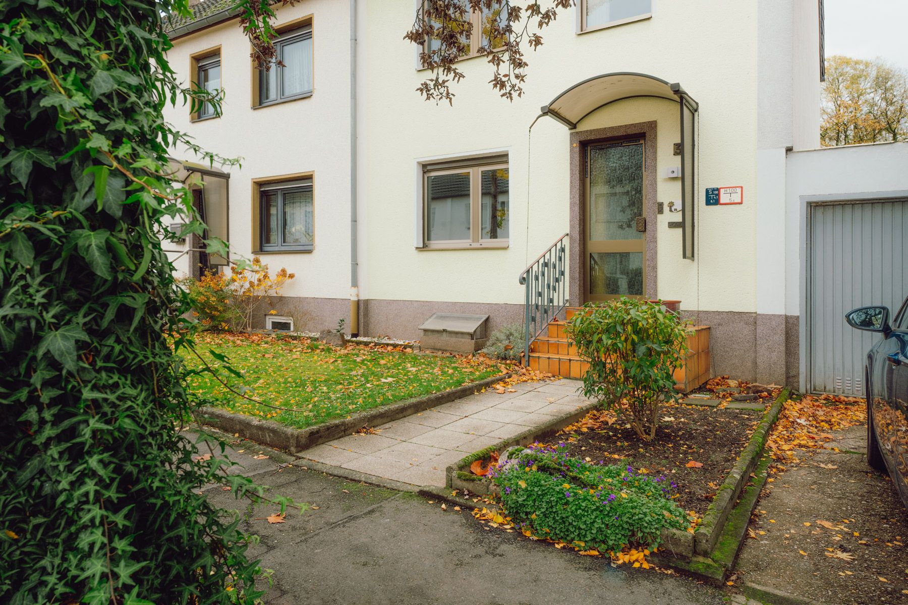 Eingang eines Wohnhauses mit Treppe, Vorgarten und Blumenbeet im Herbst.