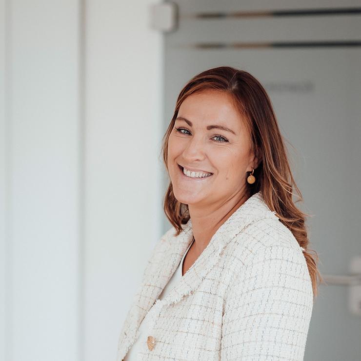 Frau mit hellbraunen Haaren sitzt und lächelt in einem hellen Raum.