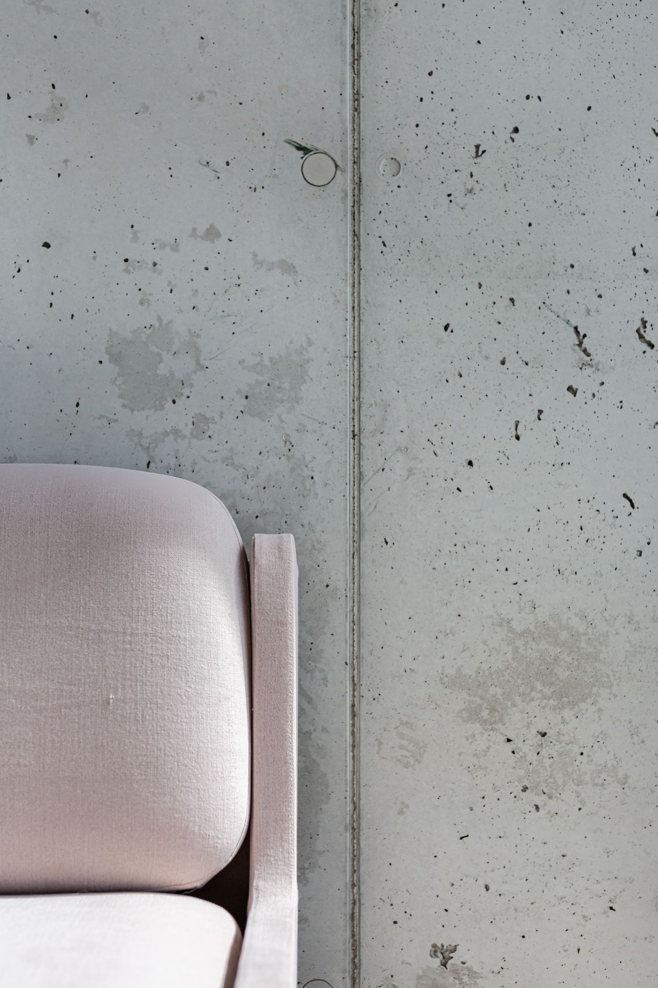 Linke Ecke eines hellrosa Sofas vor einer grauen Betonwand.