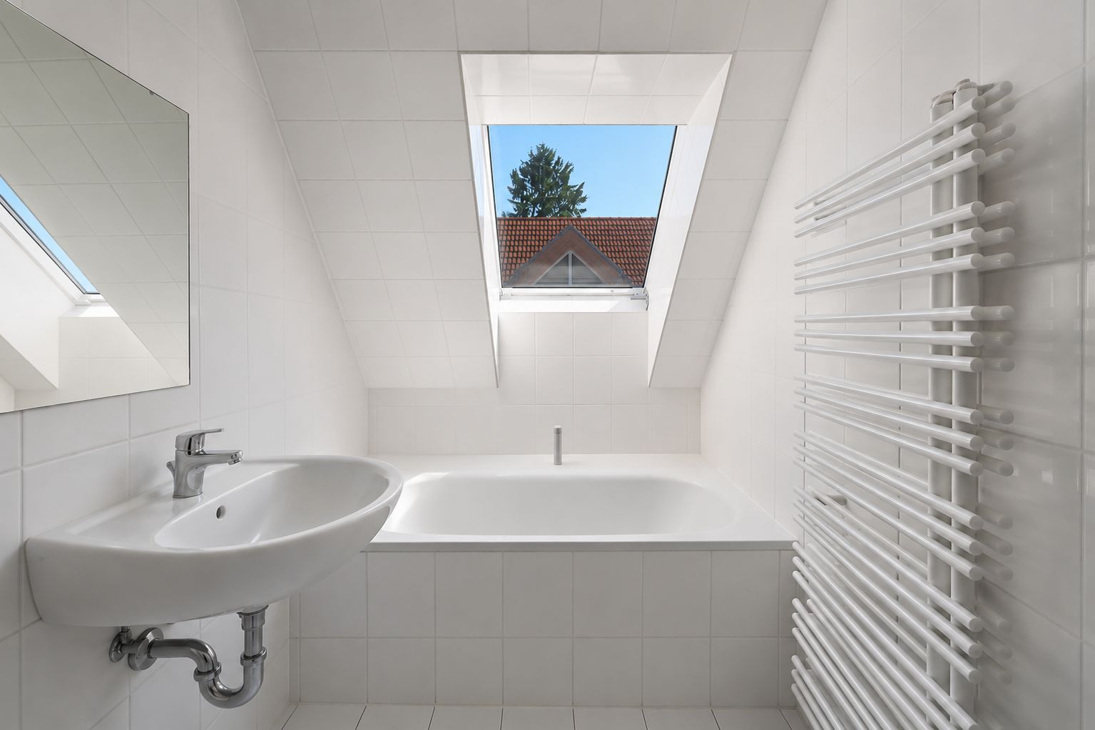 Helles Badezimmer mit Dachfenster, Badewanne, Waschbecken, Heizkörper und Spiegel.