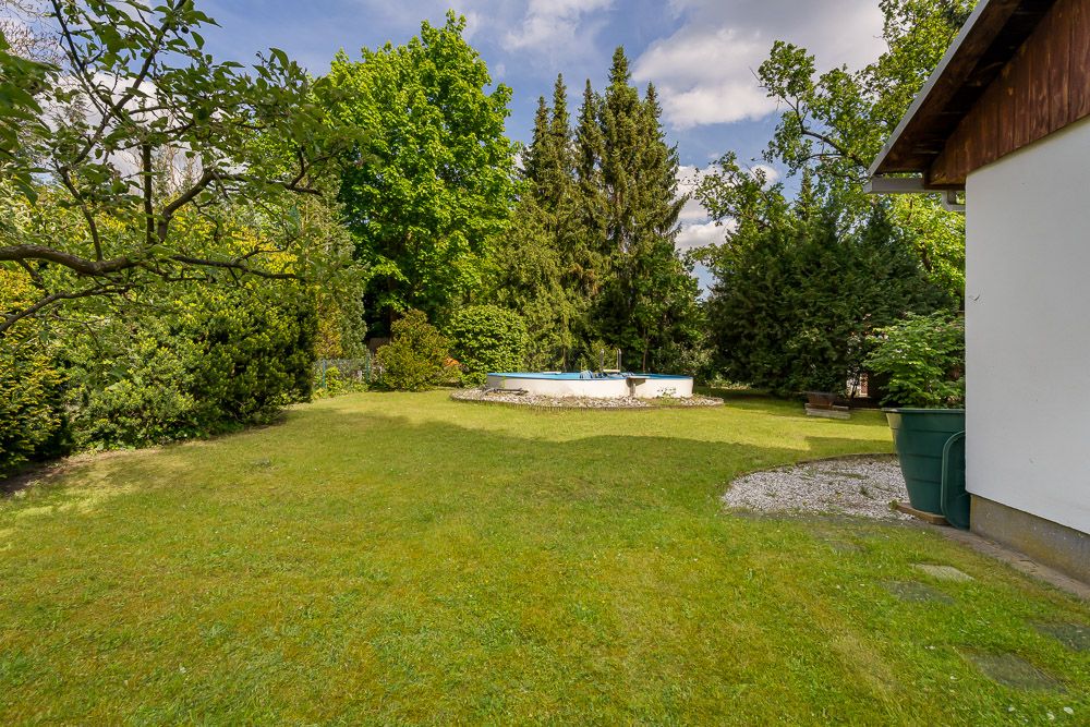 Garten mit Rasenfläche, rundem Pool und vielen Bäumen im Hintergrund.