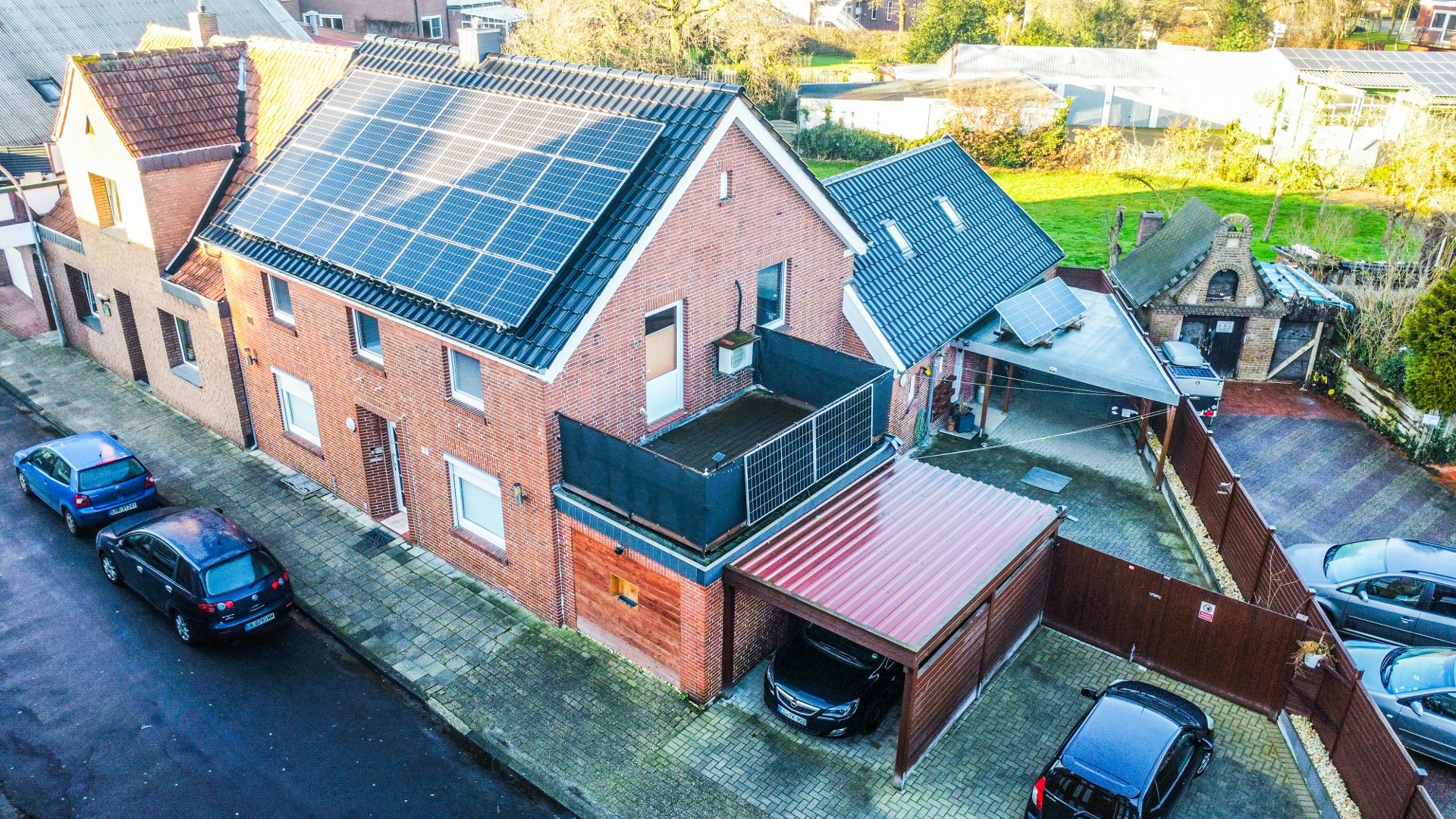 Backsteinwohnhaus mit Solarpanels auf dem Dach, Carport und geparkten Autos.