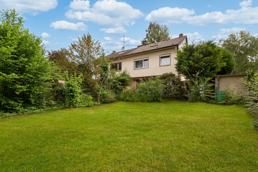 Zweistöckiges Wohnhaus mit großem Garten und vielen Bäumen im Hintergrund.