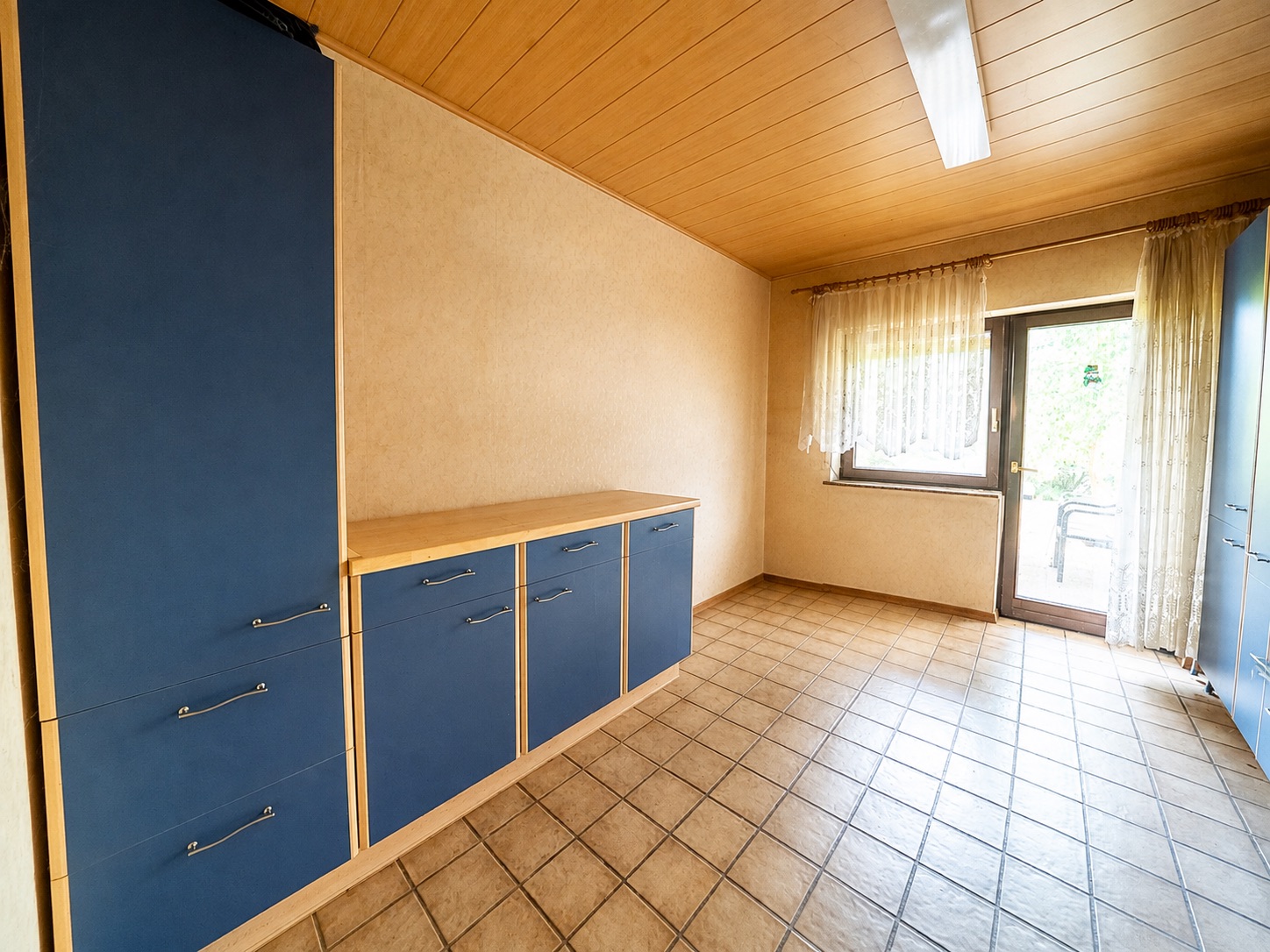 Leerer Raum mit blauen Schränken, Fliesenboden und Fenster mit Vorhang.