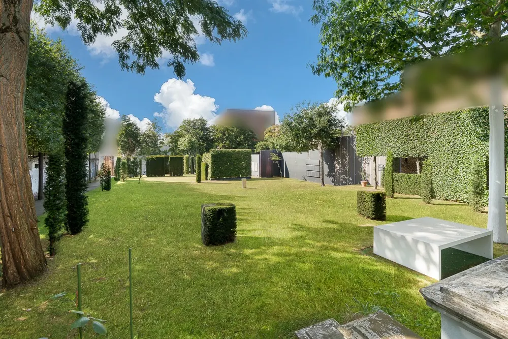 Großer, gepflegter Garten mit Rasen, Hecken, Bäumen und modernen Sitzbänken.