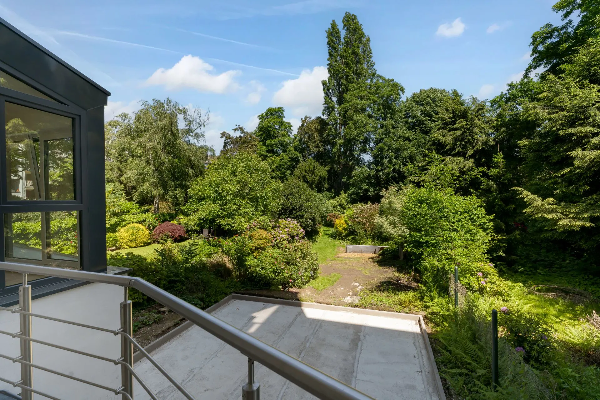 Blick von einem Balkon auf einen grünen Garten mit vielen Bäumen und Sträuchern.
