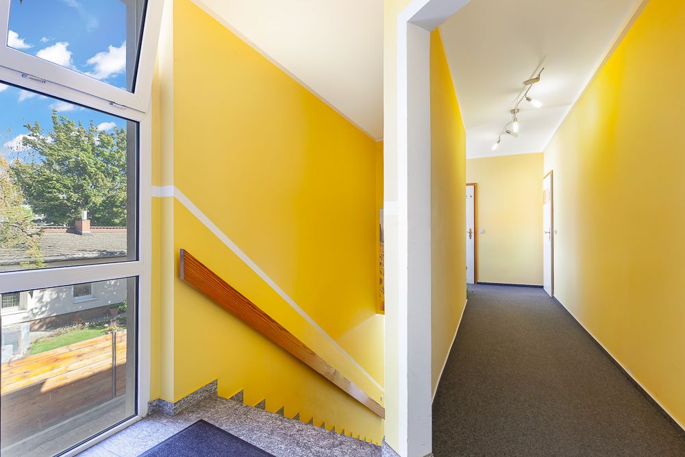 Heller Flur mit gelben Wänden, Treppe und großem Fenster mit Blick nach draußen.