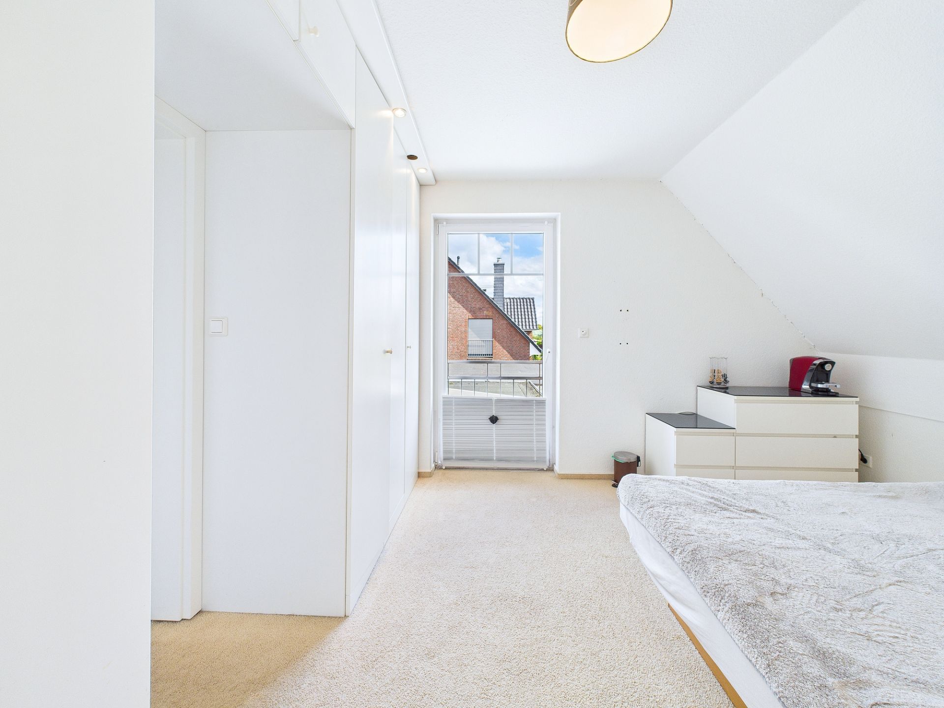 Helles Schlafzimmer mit weißem Kleiderschrank, Bett und Fenster mit Blick nach draußen.