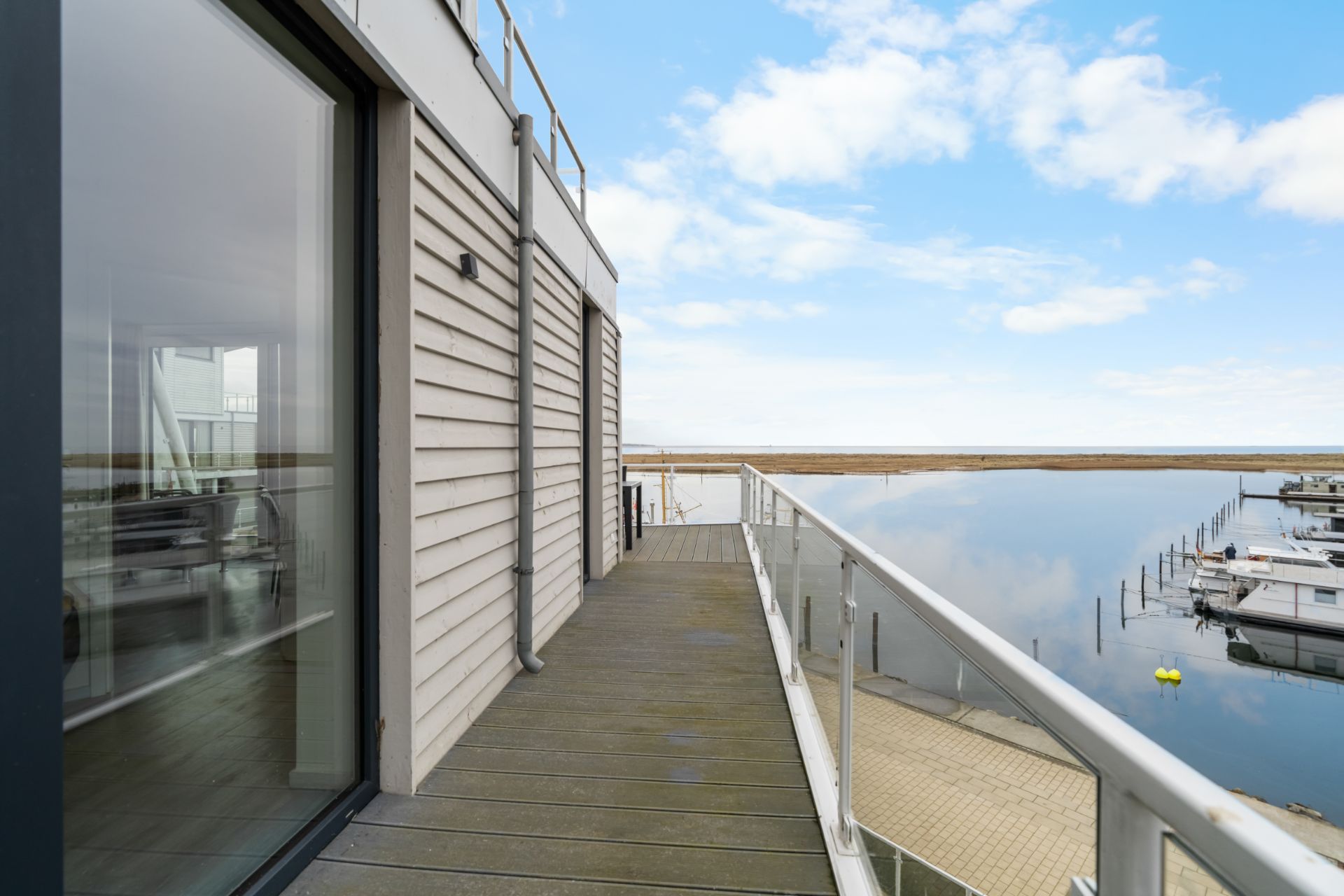 Balkon mit Glasgeländer und Blick auf ruhiges Wasser und Boote.