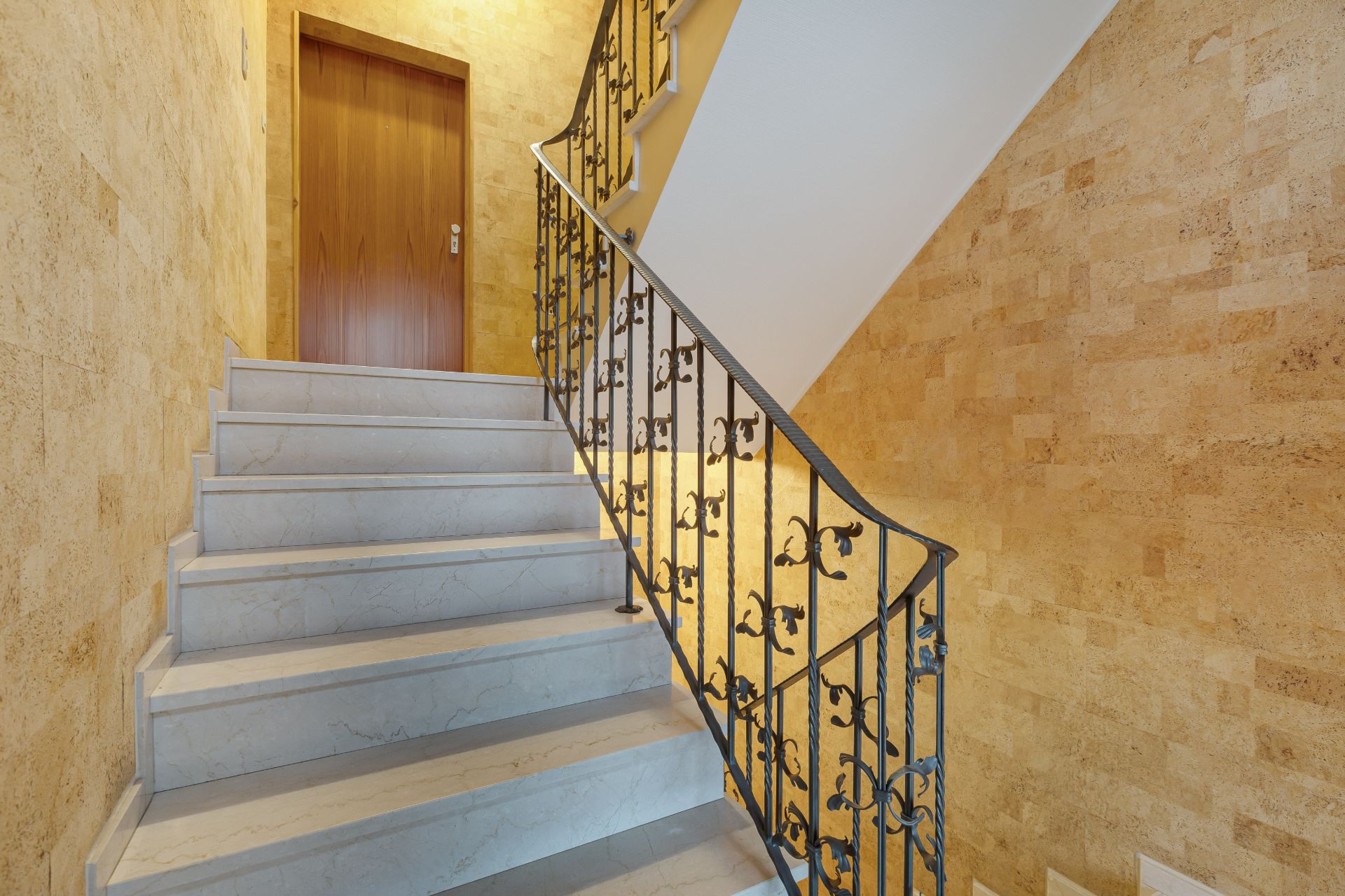 Treppenhaus mit Marmorstufen, metallischem Geländer und Holztür oben.